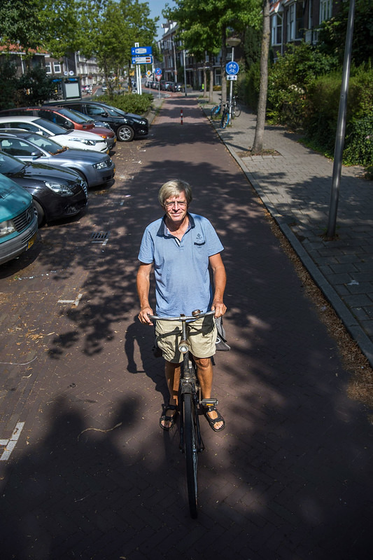 Jan Ploeger em sua bicicleta em uma ciclovia ladeada por calçamento e estacionamento de carros.
